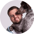 Man smiling while hugging a dog against a grey background.