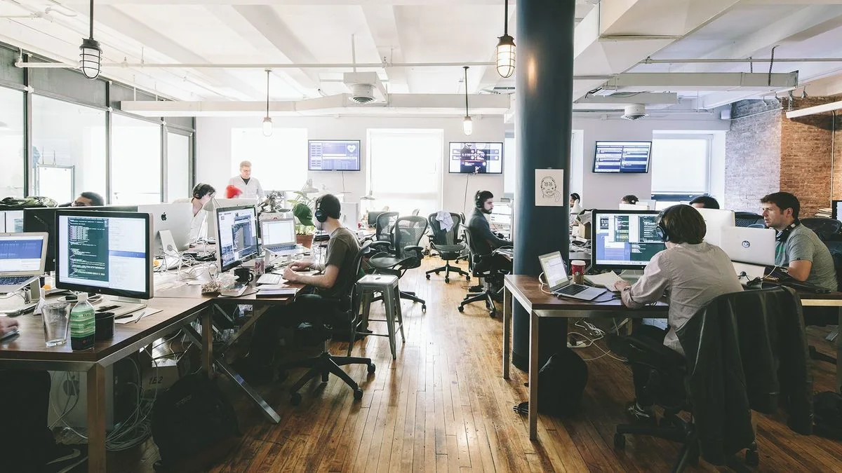 Modern open office with people working at computers, bright and collaborative space.