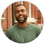 Man in green shirt smiling against brick wall background.